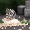 Elegant silver snake ring with crossover design, displayed on natural stone and floral background
