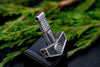 Thor's Hammer pendant against white flower and leaf background, highlighting handcrafted silver finish.