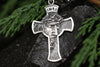 Religious cross necklace with oxidized silver finish photographed on light surface with natural greenery accents